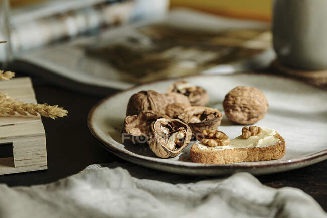 Pane tostato con burro e noci aperte su un piatto in un accogliente tavolo di legno al mattino — Foto stock