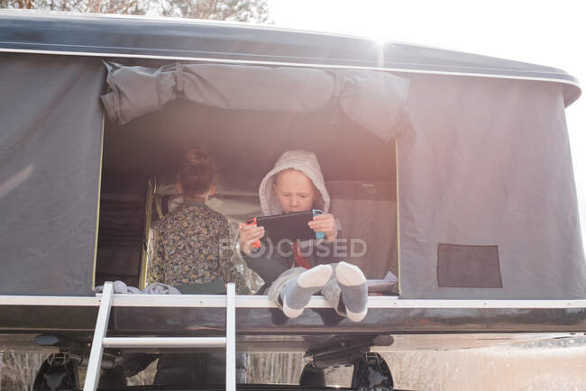 Boy sat playing a Nintendo games console in a roof top tent camping — Stock Photo