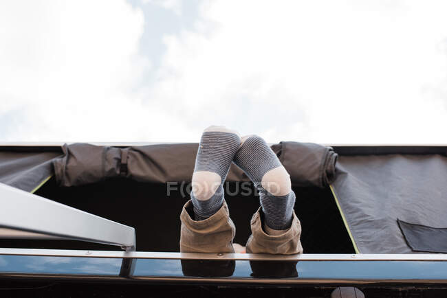Pies de niño colgando de una tienda de campaña en la azotea mientras acampa - foto de stock
