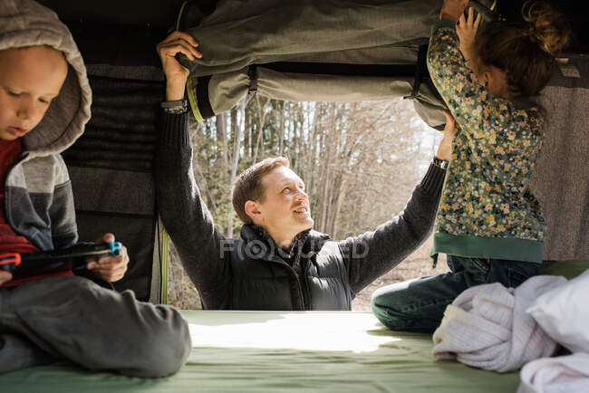 Отец устанавливает палатку на крыше со своими детьми для социальной дистанции — стоковое фото