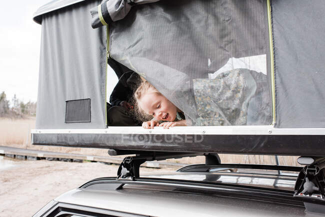 Young girl playing in a roof top tent whilst camping — Stock Photo