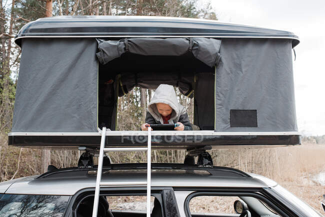 Menino jogando Nintendo em uma tenda no telhado enquanto acampando — Fotografia de Stock