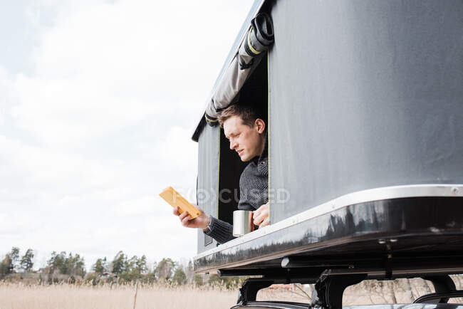 Man reading his kindle whilst social distancing in a tent with a view — Stock Photo