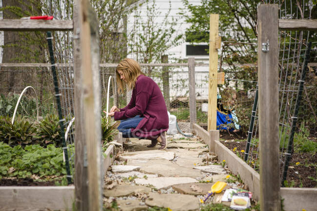 Uma mulher planta sementes em seu jardim enquanto a criança brinca no fundo — Fotografia de Stock