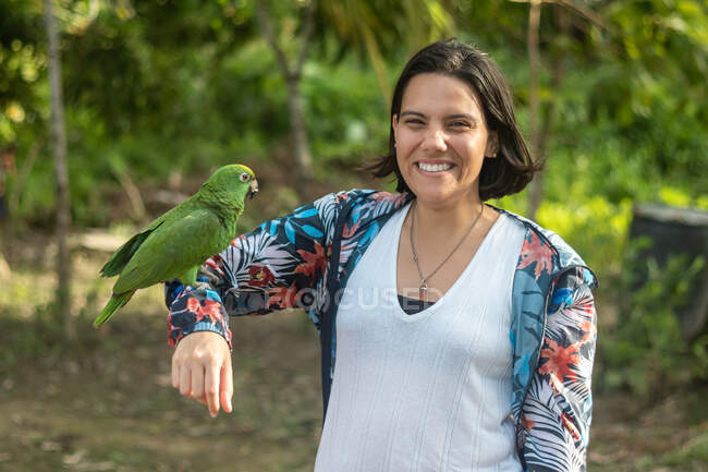 Woman poses with a smile as she carries her arm to a macaw in a camp — Stock Photo