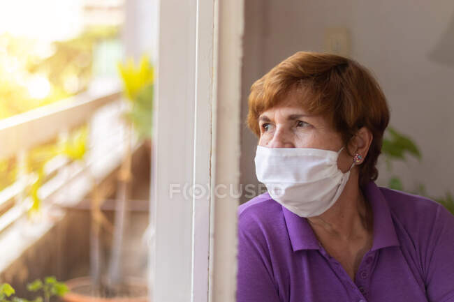 Elderly watches through the window of her house, while being confined by the coronavirus quarantine..... — Stock Photo