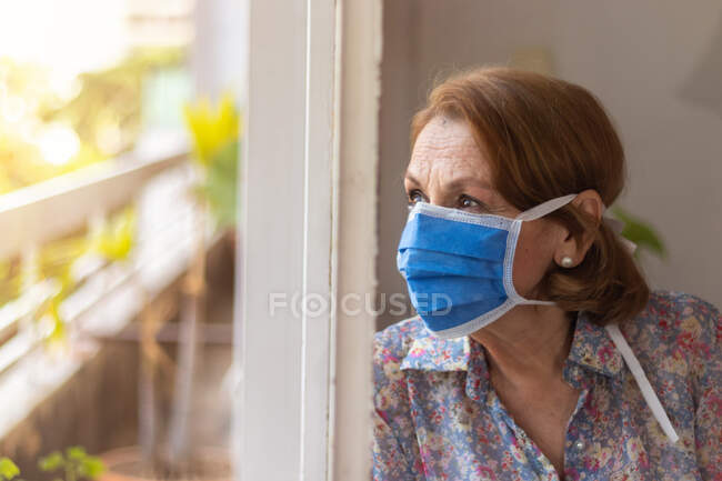 Elderly watches through the window of her house — Stock Photo