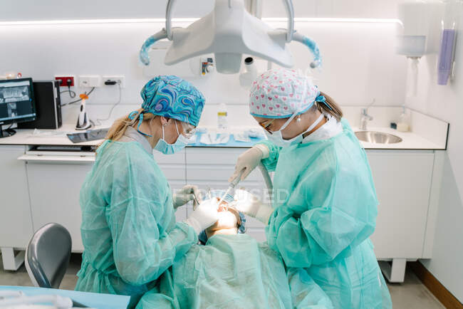 El asistente y el dentista hablan con un paciente durante una operación - foto de stock