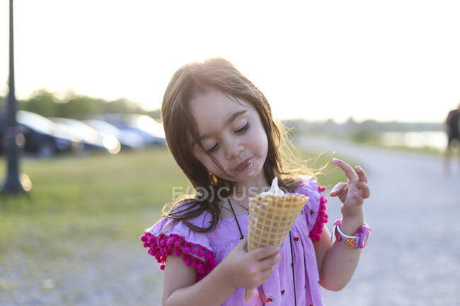 Une petite fille dans une robe rose tenant un gros cône de gaufre — Photo de stock