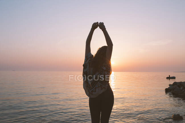 Back view of woman standing with hands above her head by the shore — Stock Photo