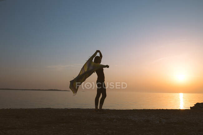 Силуэт женщины размахивая шарфом, стоя на берегу на пляже — стоковое фото
