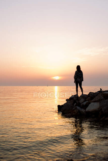 Frauensilhouette steht auf einem Felsen am Meer — Stockfoto