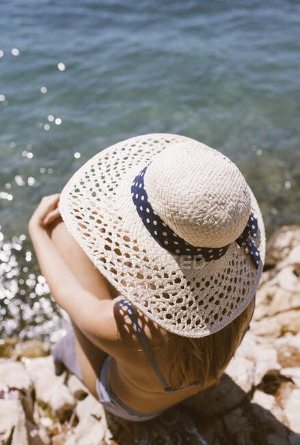 Frau mit Hut sitzt am Strand am Meer — Stockfoto