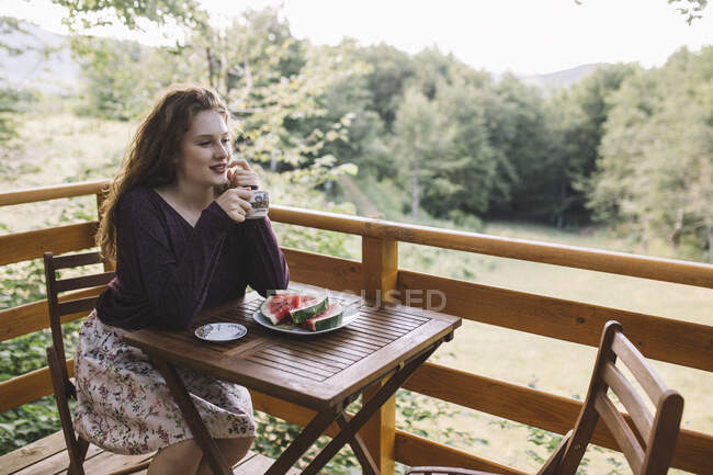 Mujer joven bebiendo café en la casa de madera balcón - foto de stock