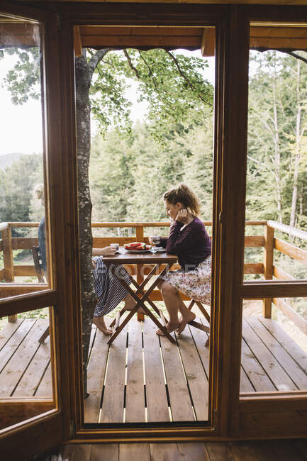 Zwei junge Frauen trinken Kaffee und essen Wassermelone auf Balkon — Stockfoto