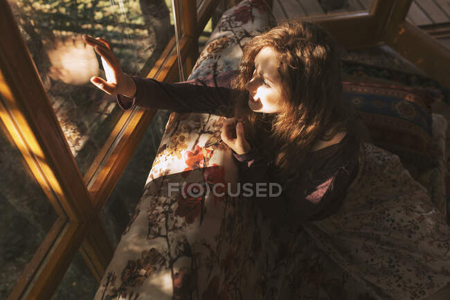 Jovem ruiva sentada no sofá e olhando através da janela — Fotografia de Stock