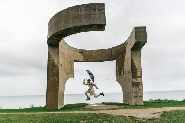 Eccitato silhouette uomo saltando con ombrello contro il tempo appannato — Foto stock