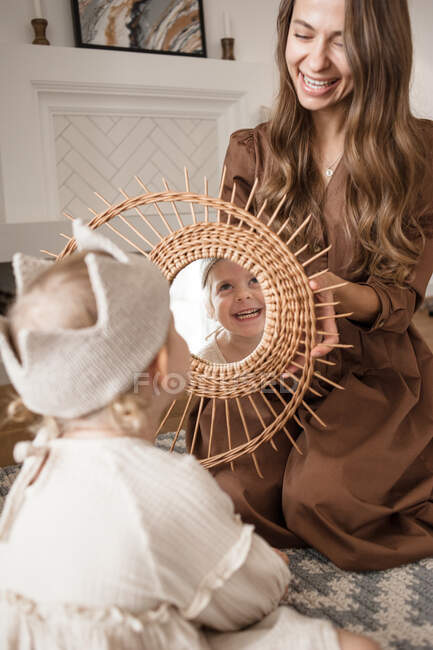 Mother holds mirror in which her laughing daughter is reflected — Stock Photo
