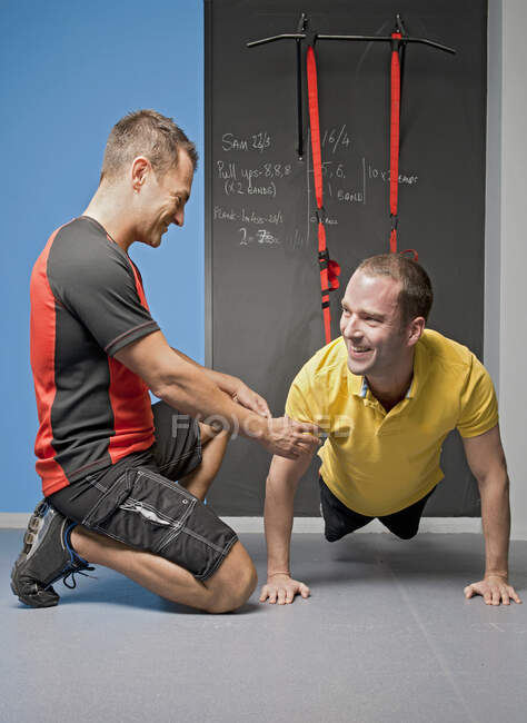 Entrenador personal ayudando al cliente con el entrenamiento de suspensión en el gimnasio - foto de stock