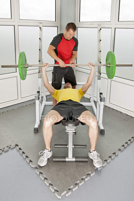 Entraîneur personnel aidant client dans la salle de gym — Photo de stock
