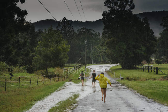 Dos chicas y un chico jugando bajo la lluvia después de un ciclón - foto de stock