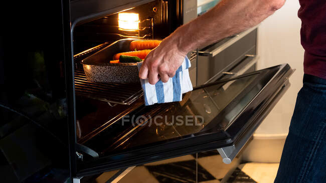 Man putting baking tray with vegetables into oven to roast. Healthy food concept — Stock Photo