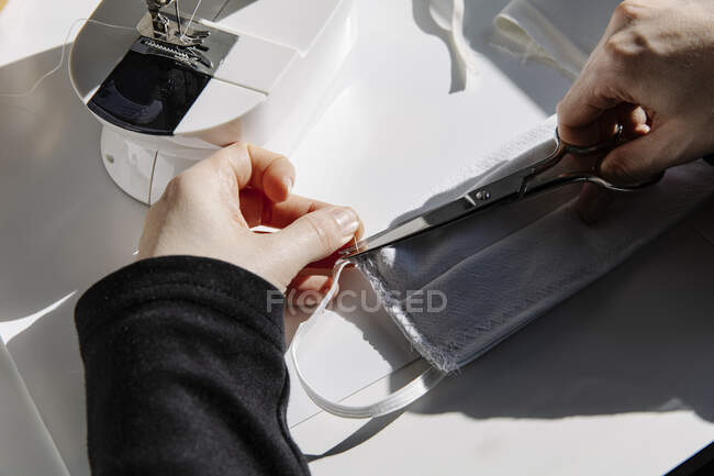 Faceless woman sewing and cutting thread in a handmade mask at home — Stock Photo