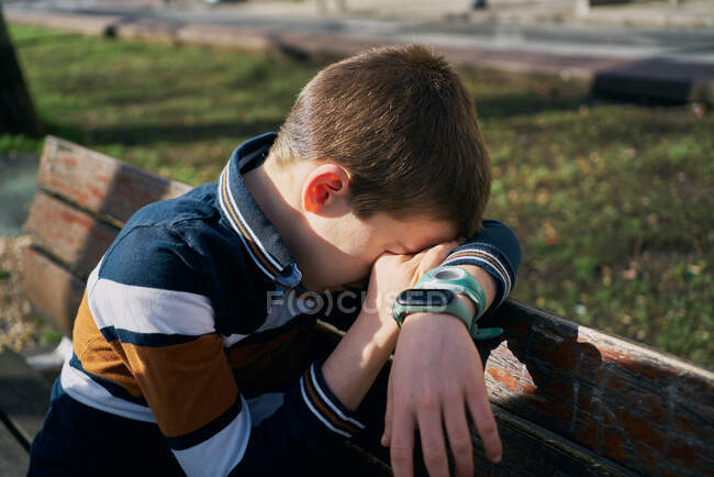 Ребенок на скамейке закрывает лицо рукой и плачет — стоковое фото