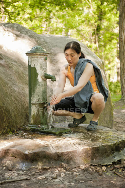 Mujer lavándose las manos en la bomba de agua en el bosque de Fontainebleau - foto de stock