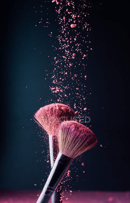 Cepillos de maquillaje con explosión de polvo violeta sobre fondo negro - foto de stock