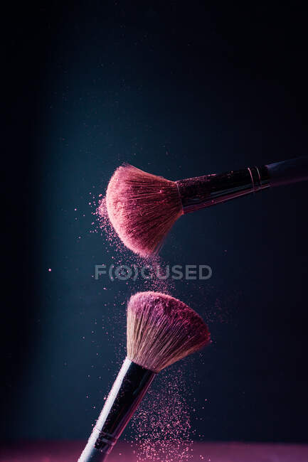 Cepillos de maquillaje con explosión de polvo violeta sobre fondo negro - foto de stock