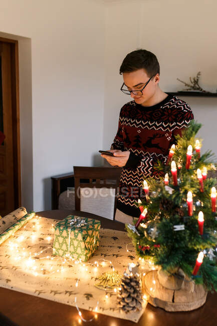 Мужчина фотографирует на смартфоне аккуратно обернутый рождественский подарок — стоковое фото
