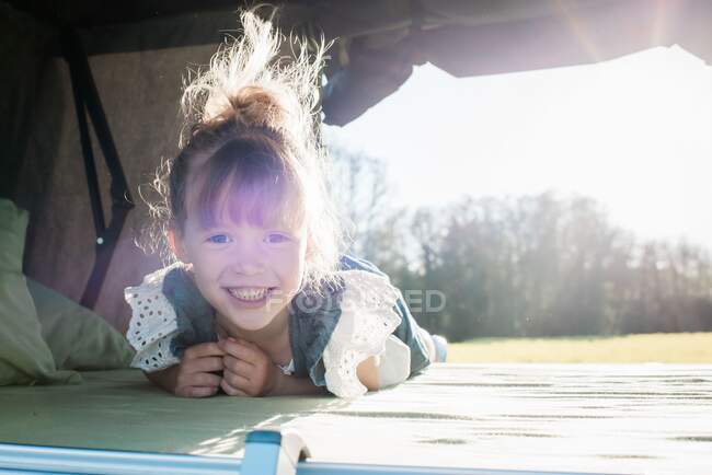 Portrait of a young girl sat in a roof top tent smiling at sunset — Stock Photo