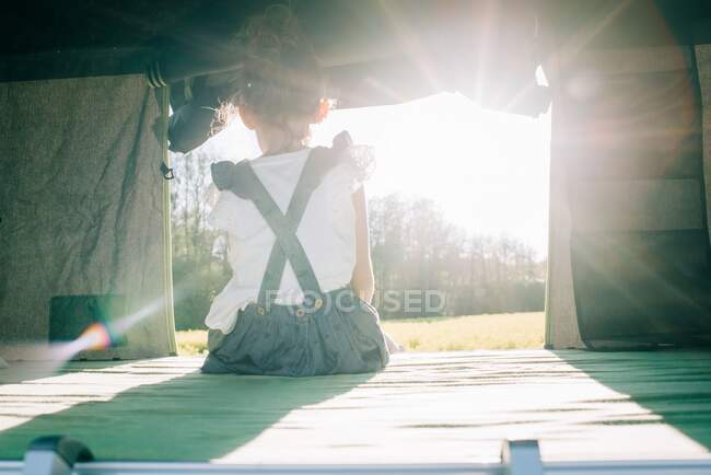Young girl sat in a tent watching the sun set whilst camping outdoors — Stock Photo