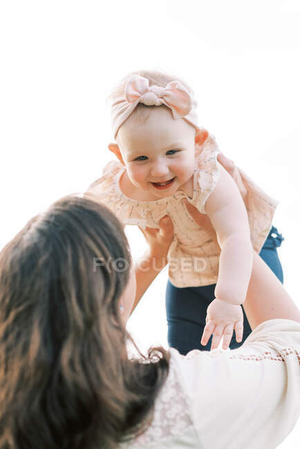 Eine süße Einjährige, die von ihrer Mutter hochgehalten wird. — Stockfoto