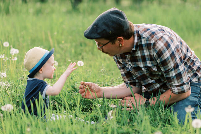 Father and son playing amid the dandelion in a grassy field — Stock Photo