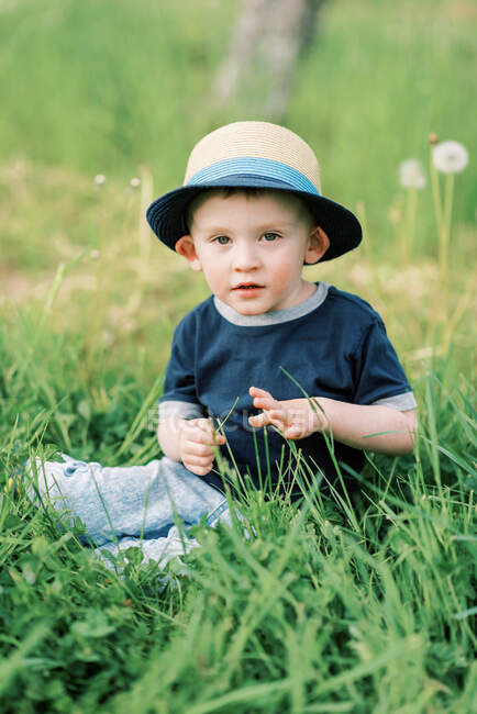 Foto stock de um menino pequeno sentado na grama alta — Fotografia de Stock