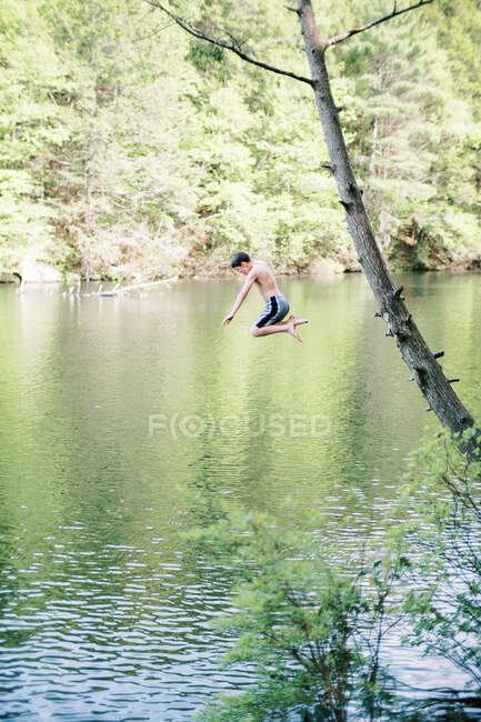 Um rapaz a saltar de uma árvore para um lago. — Fotografia de Stock