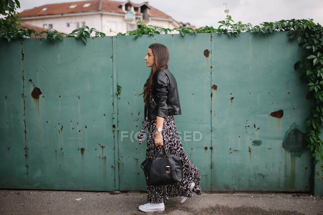 Молодая женщина в платье и кожаной куртке гуляет по городу — стоковое фото