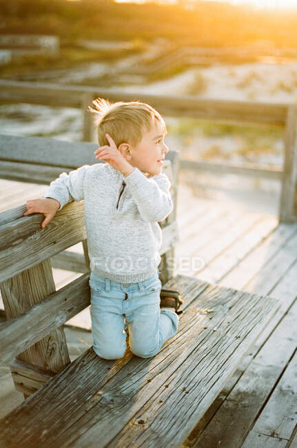 Ein kleiner Junge sitzt auf einer Bank mit Blick auf die Dünen bei Sonnenuntergang — Stockfoto