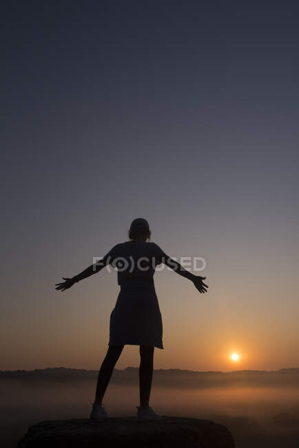 Силуэт девушки на вершине горы с вытянутыми руками на восходе солнца — стоковое фото