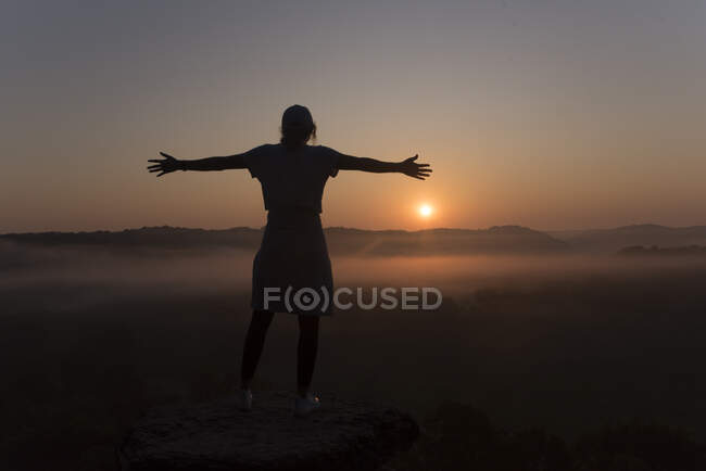 Silhouette eines Mädchens auf dem Gipfel eines Berges bei Sonnenaufgang mit ausgebreiteten Armen — Stockfoto