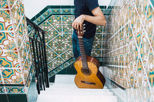 Crop man de pie en una escalera con una guitarra española. - foto de stock