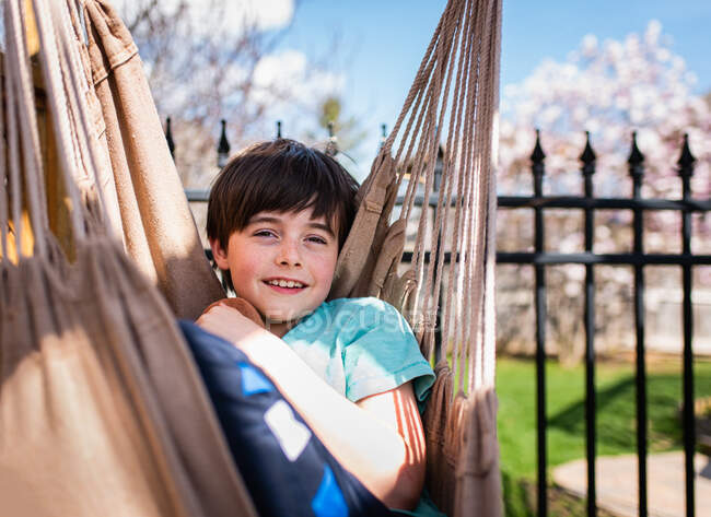 Счастливый мальчик отдыхает в гамаке на заднем дворе в летний день. — стоковое фото