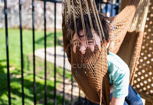 Хлопчик, який сидить у гамаку на задньому дворі літнього дня . — стокове фото
