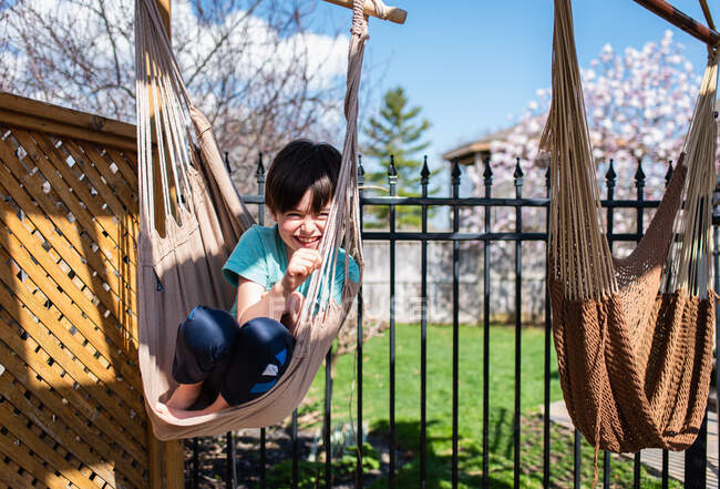 Счастливый мальчик сидит в гамаке на заднем дворе в летний день. — стоковое фото