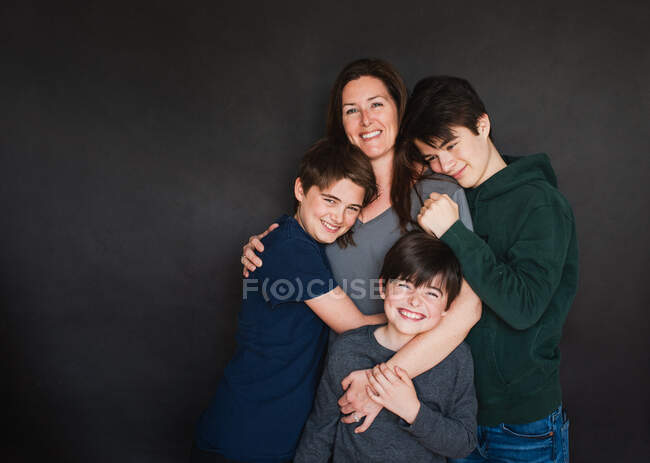 Mãe com três meninos mais velhos abraçando no fundo preto. — Fotografia de Stock