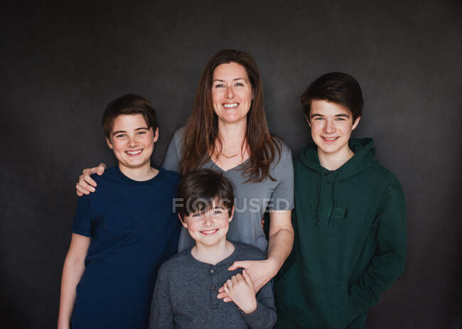 Porträt einer Mutter mit drei älteren Jungen vor schwarzem Hintergrund. — Stockfoto