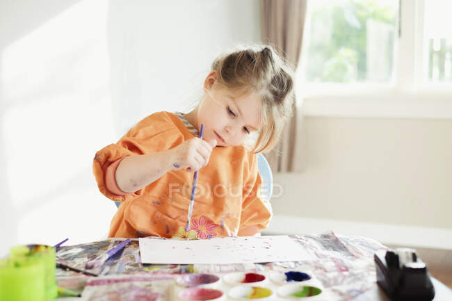 Chica joven sentada y pintando dentro - foto de stock