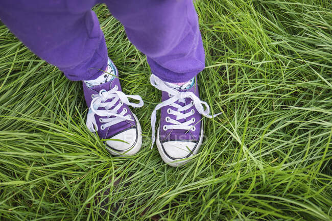 Girl wearing purple pants and shoes standing in long green grass — Stock Photo